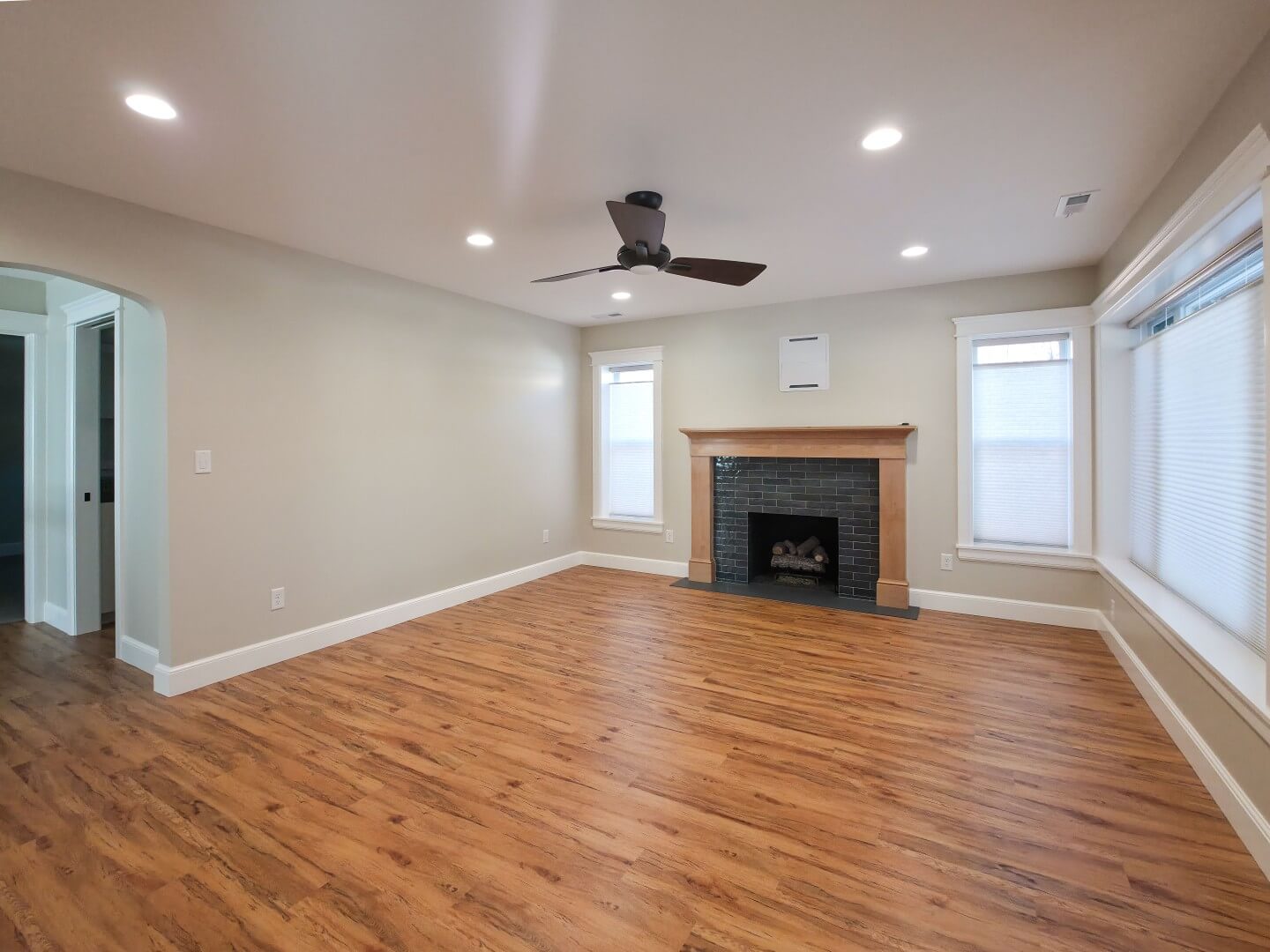 Renovated living room with a ceiling fan, updated fireplace, wood flooring, and multiple windows.