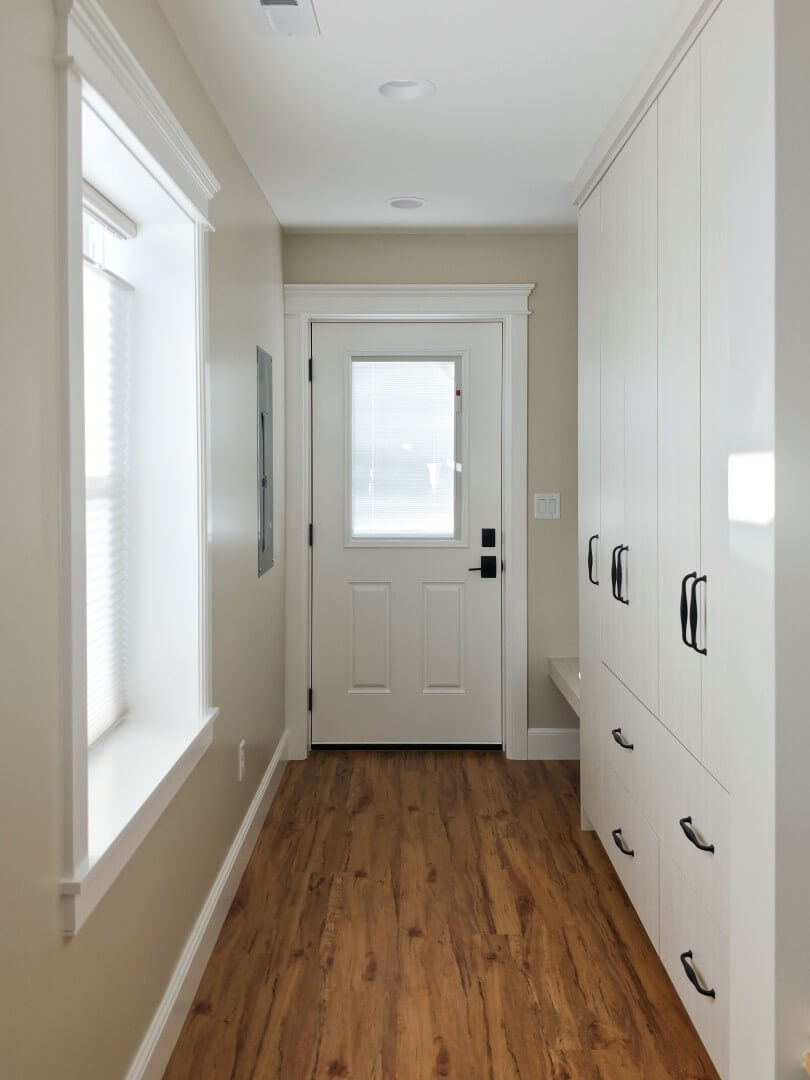 Newly created mudroom with cabinetry and a built-in bench on the right, a brand new door with access to the backyard straight ahead, and a window on the left.