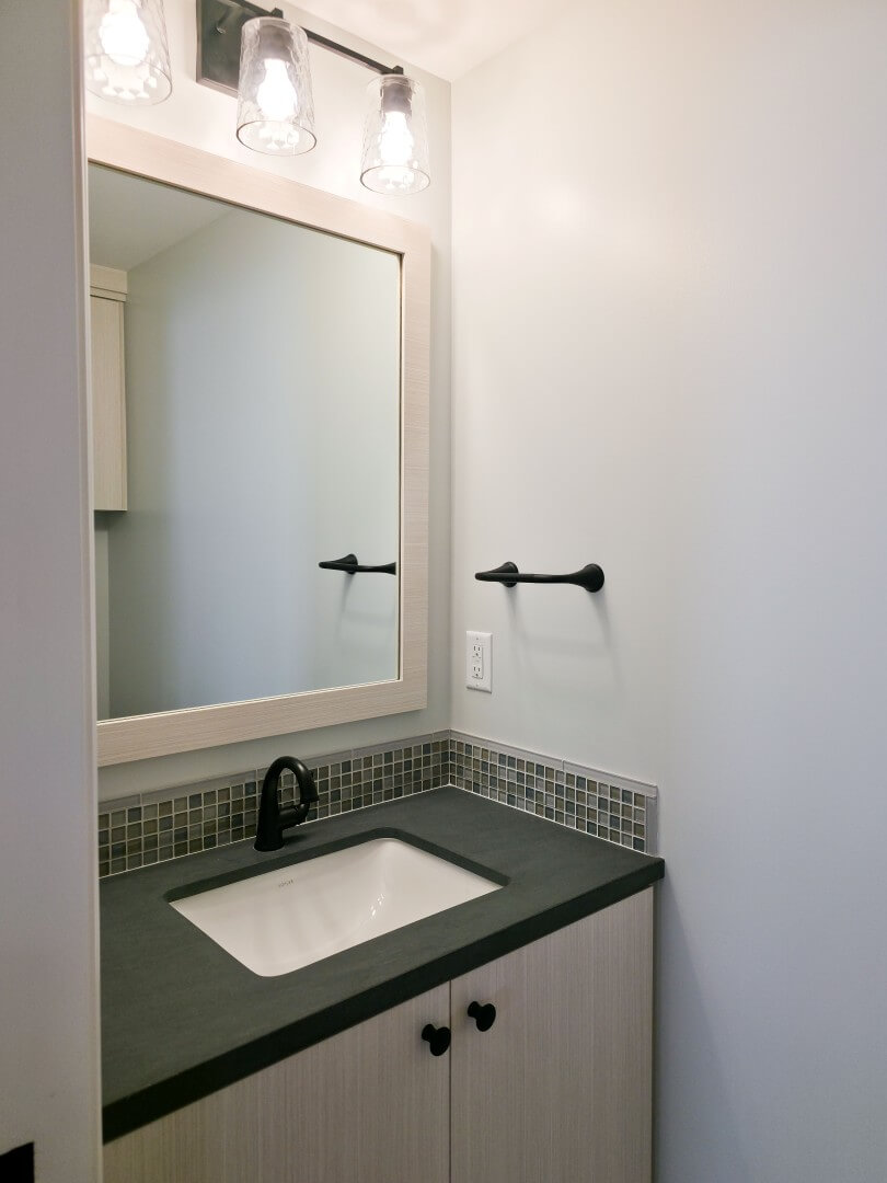 Vanity in the powder bathroom. The vanity includes storage, a small counter area around the sink, a mirror, and lighting.