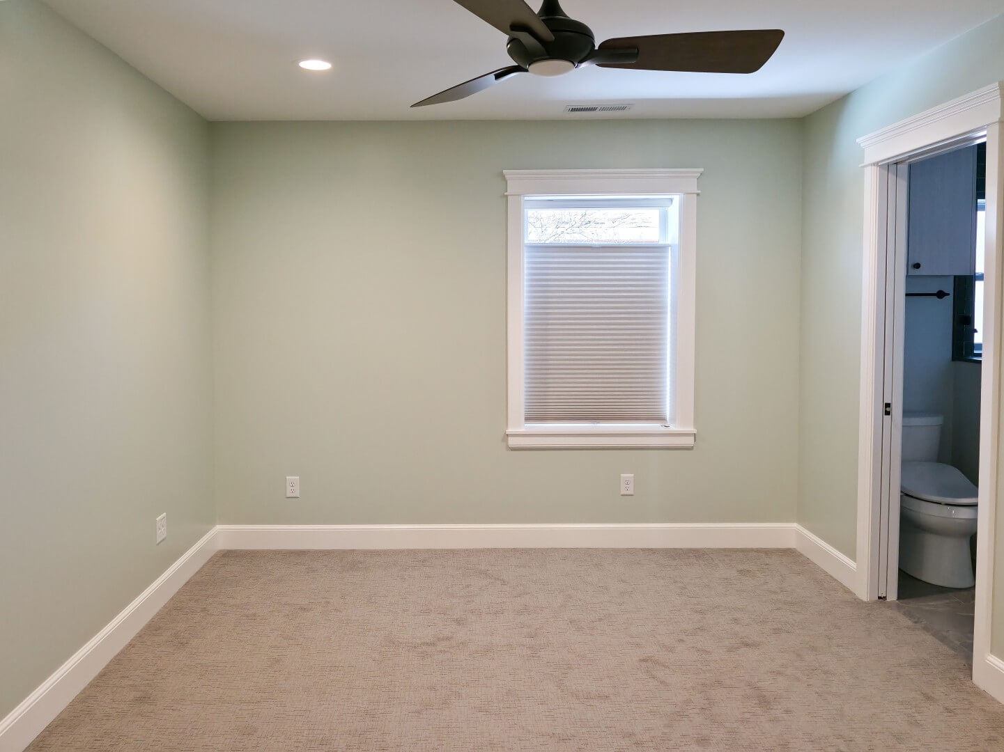 Renovated primary bedroom with carpet, a ceiling fan, and a window. On the right is a pocket door with access to the primary bathroom.