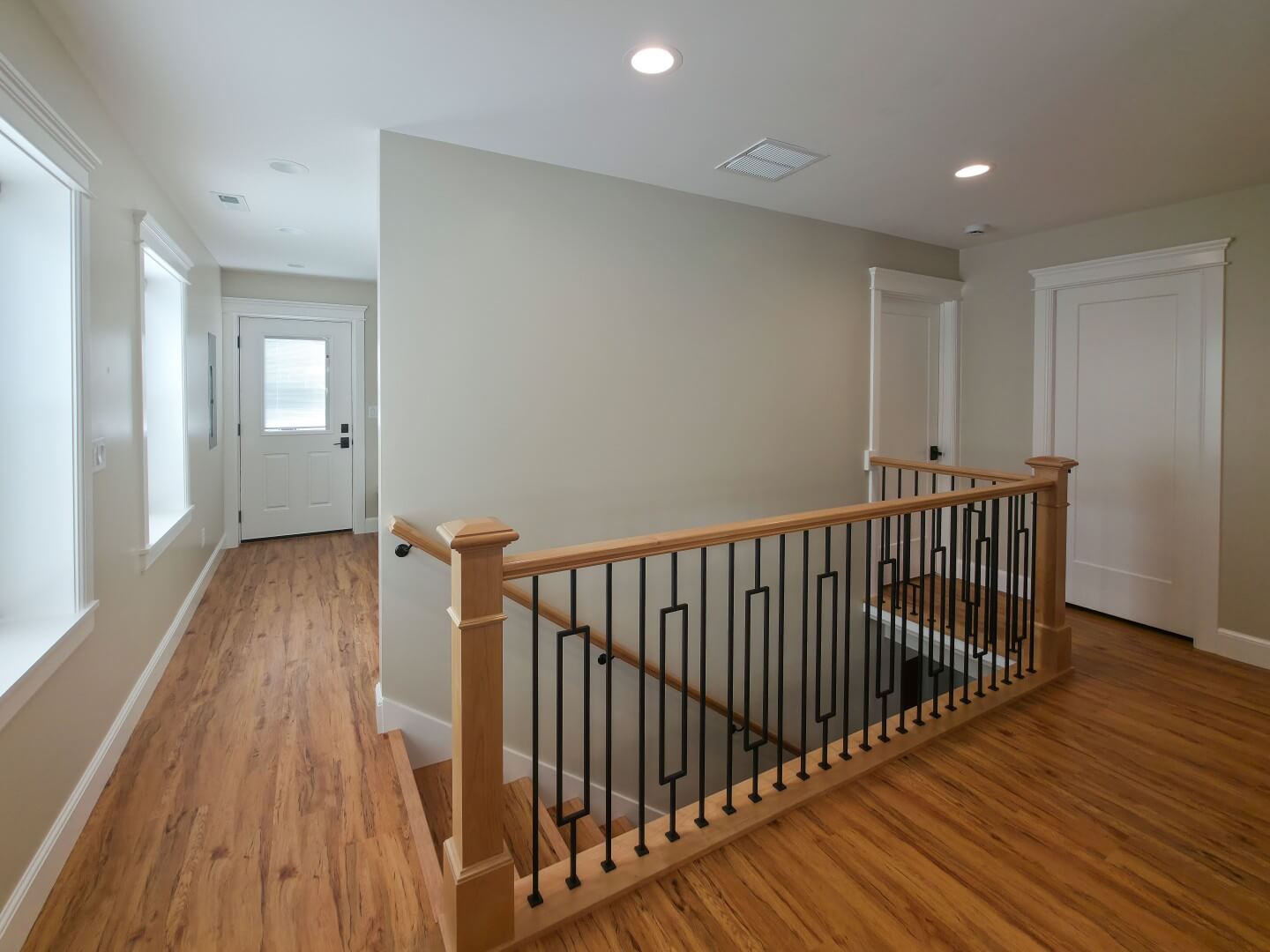 Renovated staircase with a new railing. On the left is the mudroom with a door to the backyard, and on the right are two doors with one leading to the powder bathroom and the other to the primary suite.