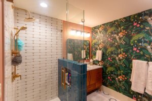 Renovated bathroom with white and blue tiles in the shower, gold fixtures, and a wallpaper that features peacocks.