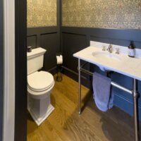 Thumbnail of http://Powder%20bathroom%20with%20a%20sink,%20a%20toilet,%20and%20wainscoting%20and%20wallpaper%20on%20the%20walls.