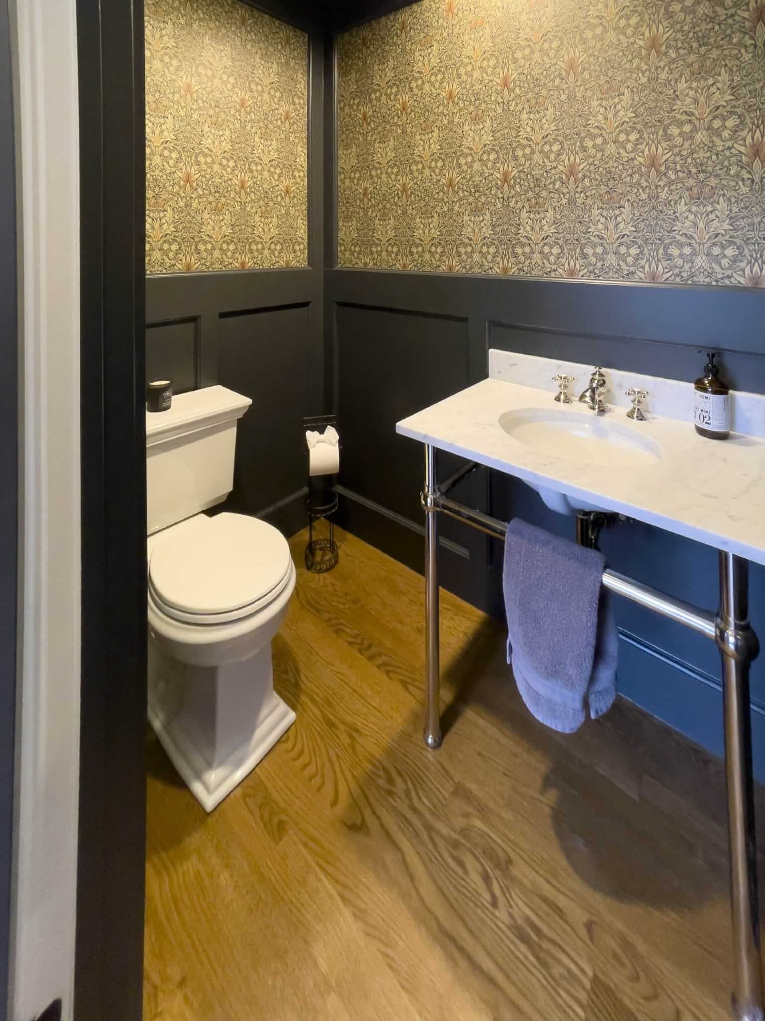 Powder bathroom with a sink, a toilet, and wainscoting and wallpaper on the walls.