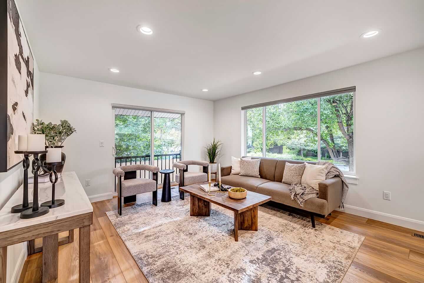 Large living room with a couch, coffee table, and two chairs. The space also includes a large window above the couch and a sliding door behind the two chairs.