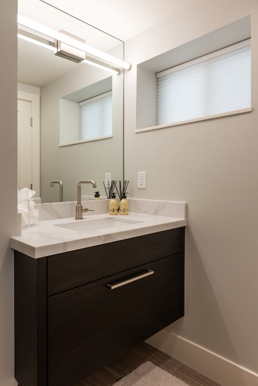 Modern bathroom vanity design. The sink is centered on the counter, includes a drawer below, and a mirror and light on the wall above. On the wall to the right, is a small window.