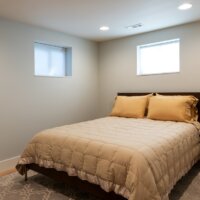 Thumbnail of http://Basement%20bedroom%20with%20two%20windows.%20The%20space%20is%20furnished%20with%20a%20large%20bed%20in%20the%20center,%20rug,%20and%20side%20table.