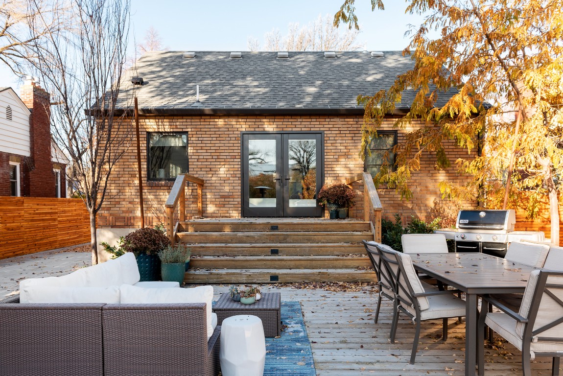 Outdoor entertaining space on a fall day. The space includes outdoor furniture, a grill, plants, and stairs up to the house.