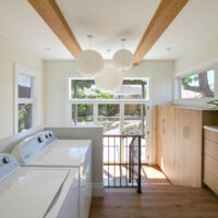 Thumbnail of http://Laundry%20room%20section%20of%20the%20addition%20looking%20toward%20the%20back%20door%20in%20the%20mudroom%20section.%20Along%20the%20left%20is%20the%20washer%20and%20dryer,%20and%20along%20the%20right%20are%20built-in%20cabinets.%20The%20space%20features%20lots%20of%20natural%20light,%20wood%20beams%20on%20the%20ceiling,%20and%20three%20round%20light%20fixtures.