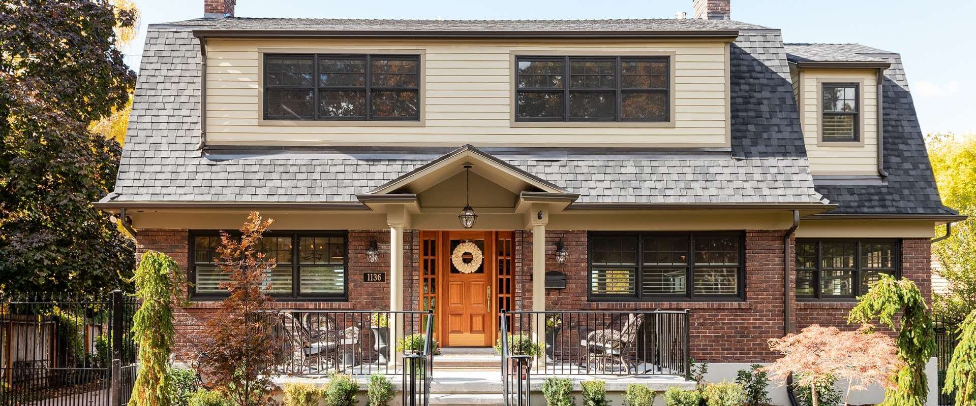 Exterior of renovated home with brick on the main level. A front porch is centered on the home.