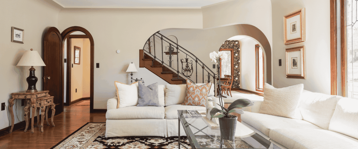 Historic home living room with arches, wood details, and a unique railing on the staircase. Furniture includes two couches, a rug, side tables, and a coffee table.