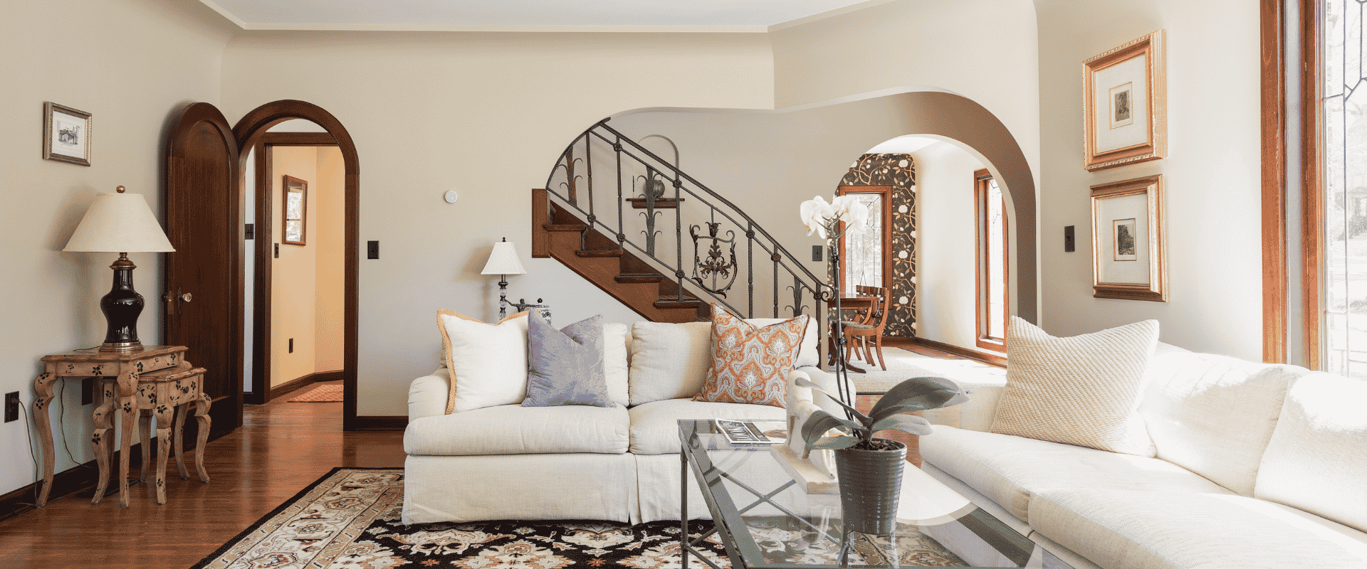 Historic home living room with arches, wood details, and a unique railing on the staircase. Furniture includes two couches, a rug, side tables, and a coffee table.