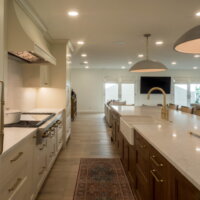 Thumbnail of http://Open%20concept%20kitchen.%20On%20the%20right%20is%20an%20island%20with%20a%20farmhouse%20sink.%20On%20the%20left%20is%20cabinetry%20and%20a%20range.