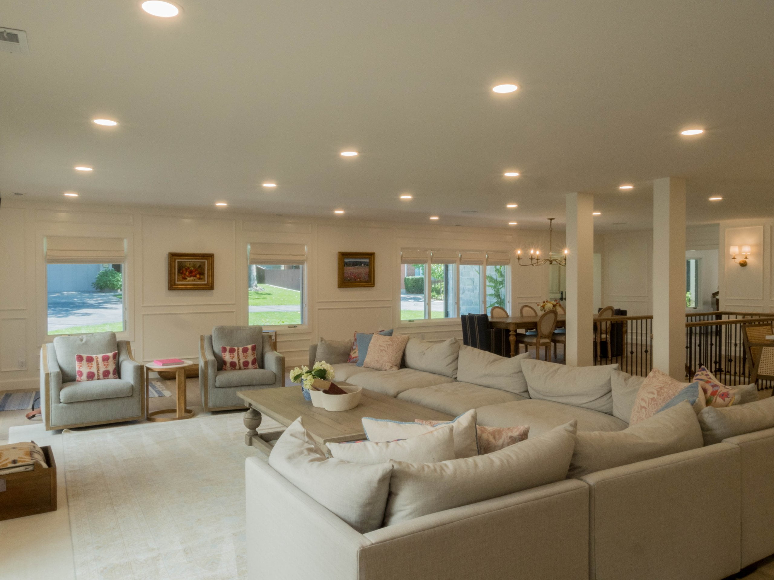 Large, open concept great room looking from the family room to the dining room. The family room includes a large L-shaped couch, two chairs with a side table between, and a coffee table.