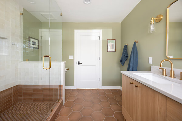 Primary bathroom with shower on the left side, entrance straight ahead, and sink on the right side. The room features green walls, hexagon tiles on the floor, and gold fixtures.