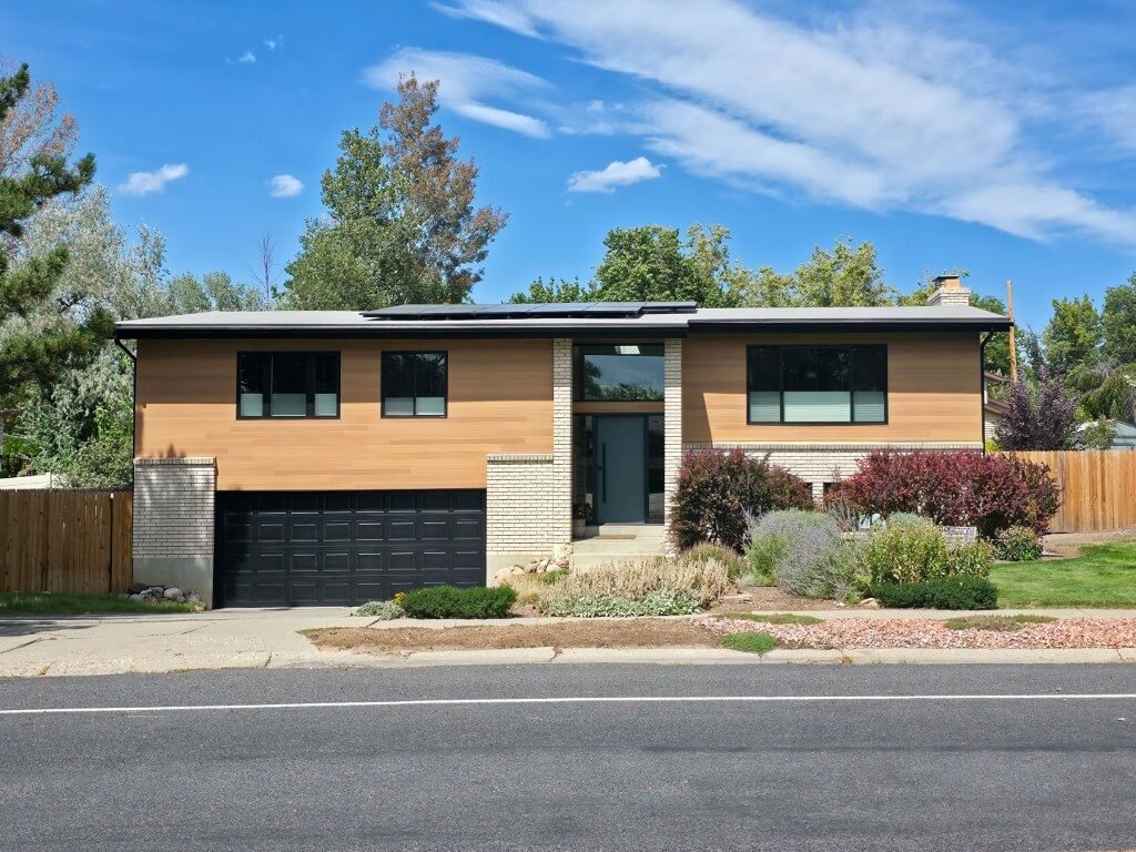 Front exterior of a split level home after the renovation. The design includes a mix of siding and brick with the front door in the center, and a garage on the left.