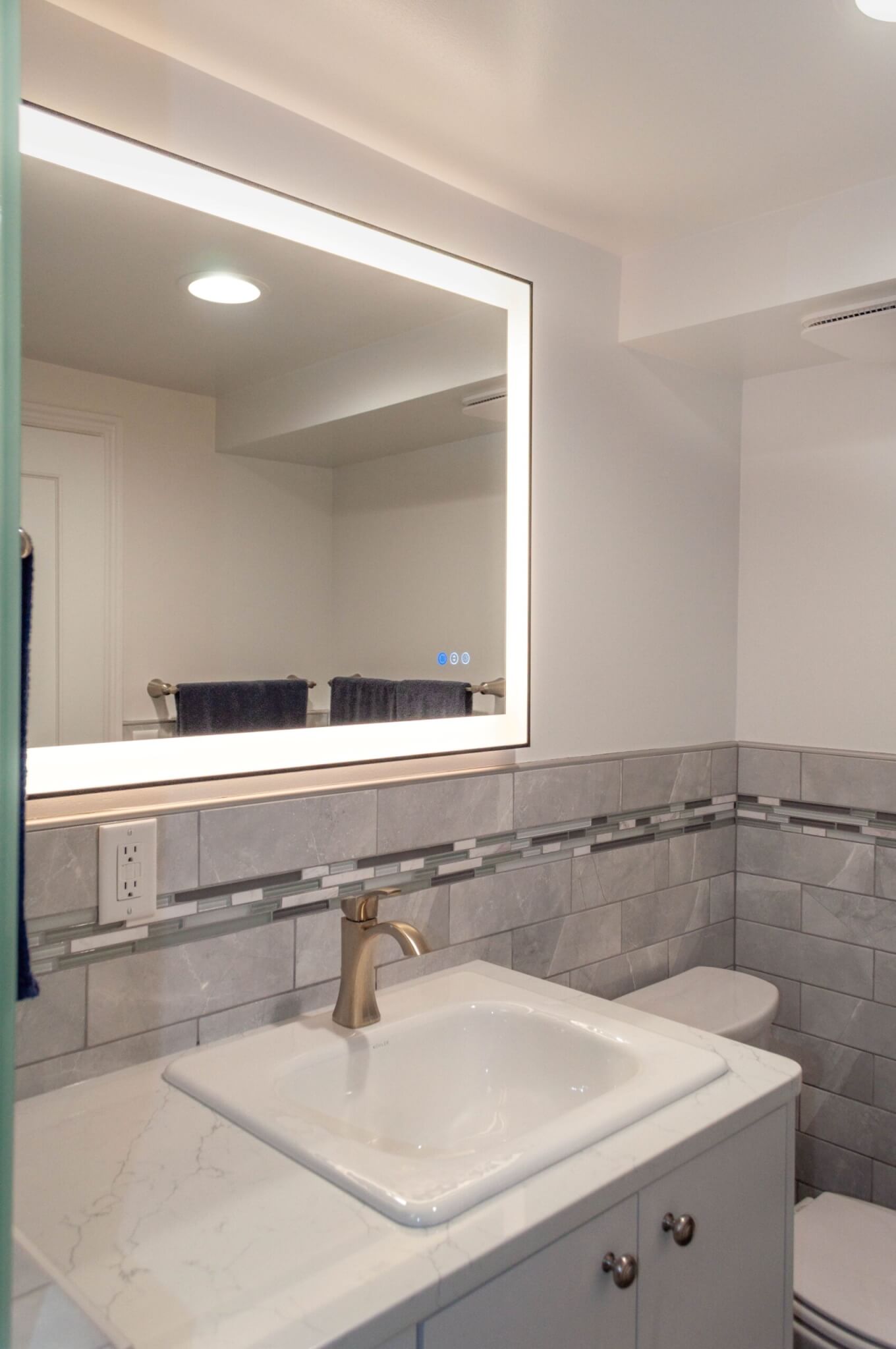 Bathroom toilet and vanity with a mirror light centered above.