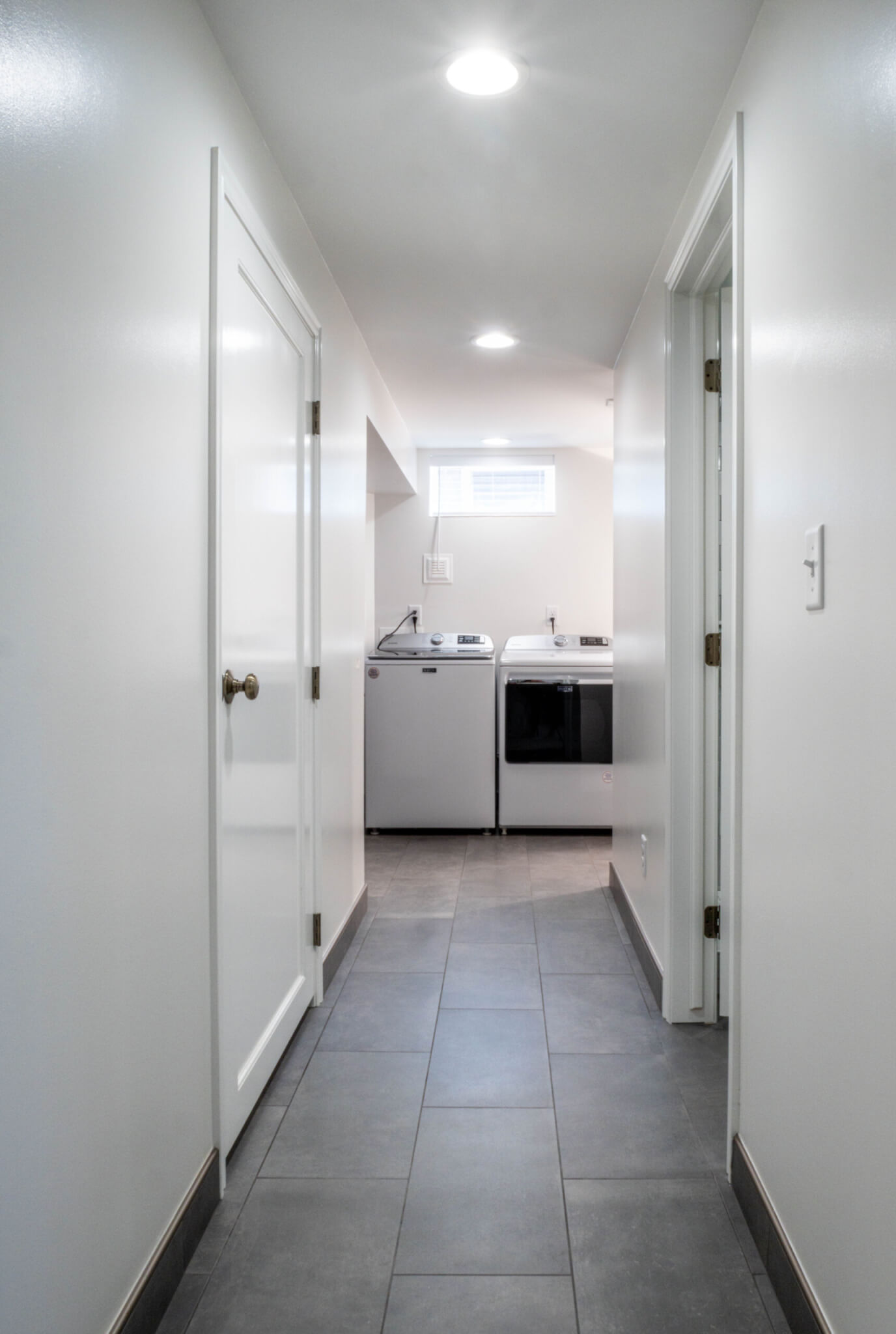 Hallway leading to the laundry room with tile flooring and white walls.