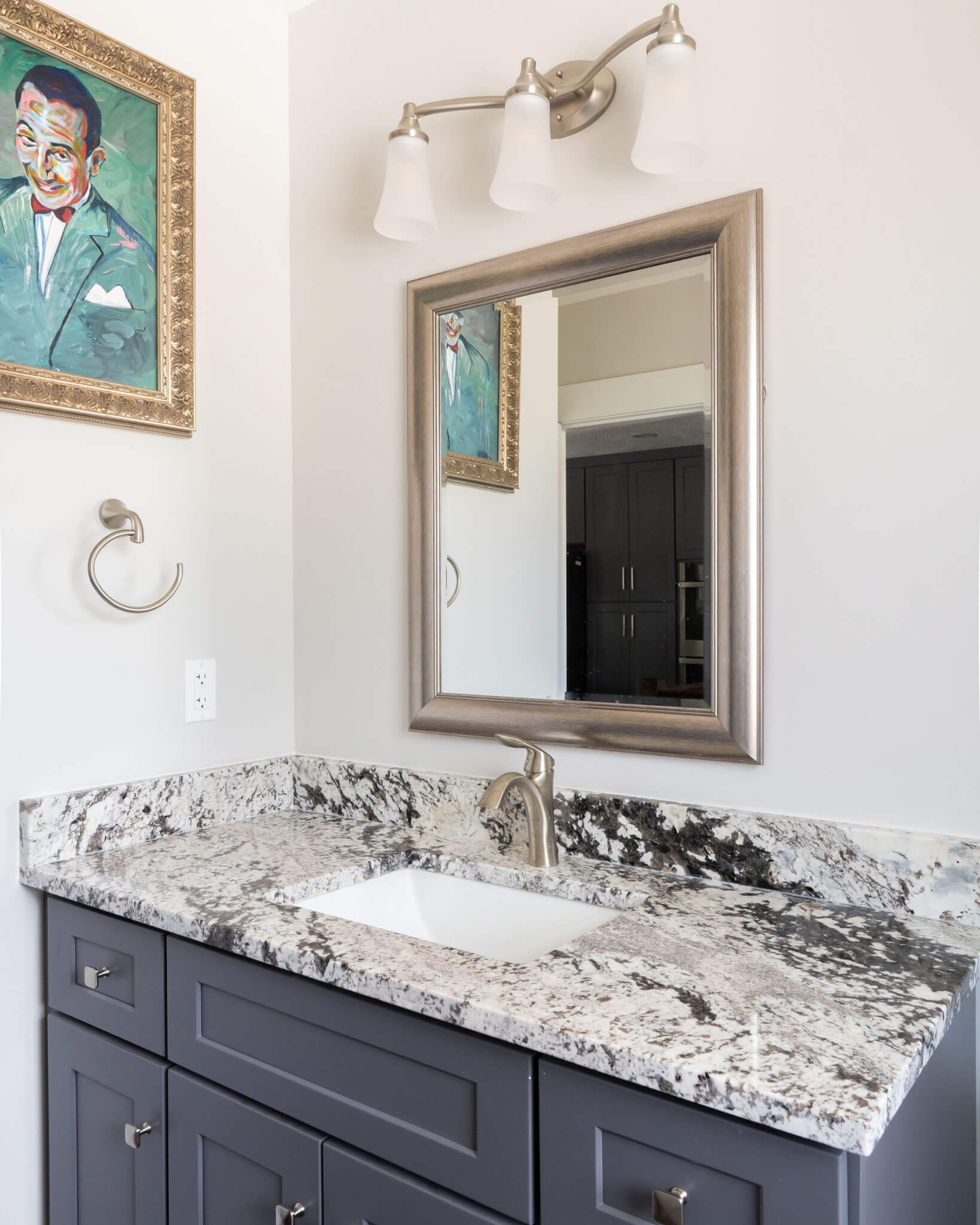 Powder bathroom vanity with a mirror and light above. On the wall to the left, is a picture and a hook to hang a towel.