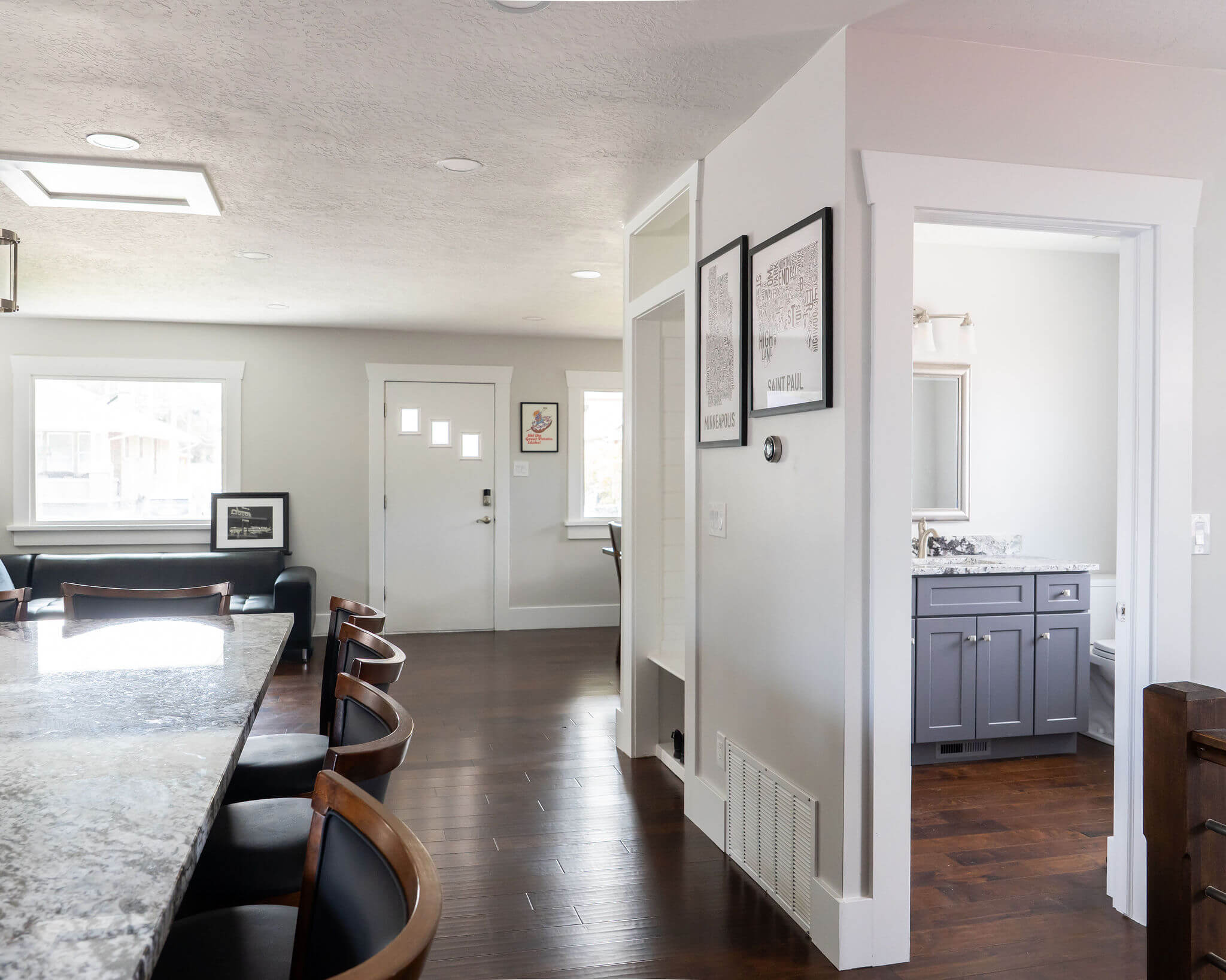 Open concept great room looking from the kitchen to the front door. On the left is a small peek to the kitchen, and on the right is a hallway and door to the powder bathroom.