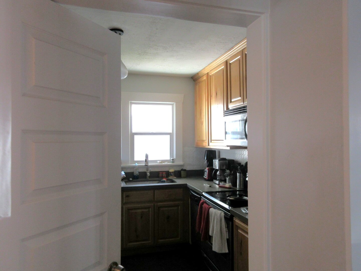 Small, enclosed kitchen before the remodel. A door is open with access to the kitchen, and a window provides light above the sink.
