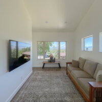 Thumbnail of http://Area%20rug%20with%20a%20couch%20facing%20toward%20the%20TV.%20In%20front%20of%20the%20windows%20is%20a%20bench%20with%20plants.