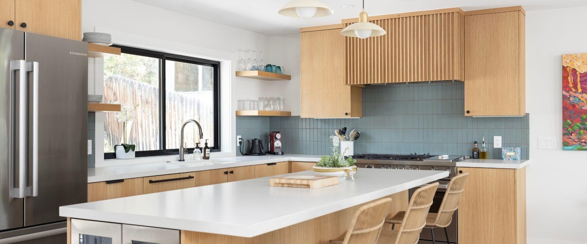 Kitchen renovation with wood cabinetry, a mix of floating shelves and upper cabinets, a large island with seating, and a sink under a large window.