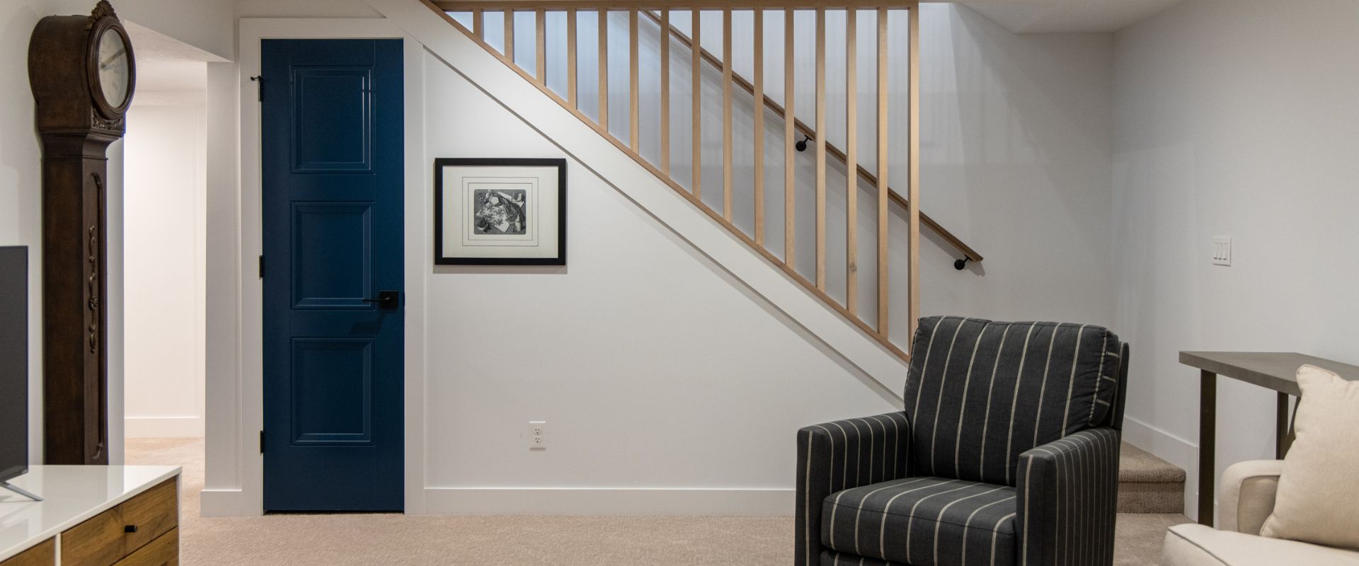 Basement family room with stairs. Under the stairs is a narrow door with access to storage.