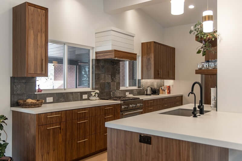 Contemporary kitchen design with a galley layout that is partially open to the living room. The kitchen includes windows on either side of the stove, vaulted ceilings, and a range with a hood above.