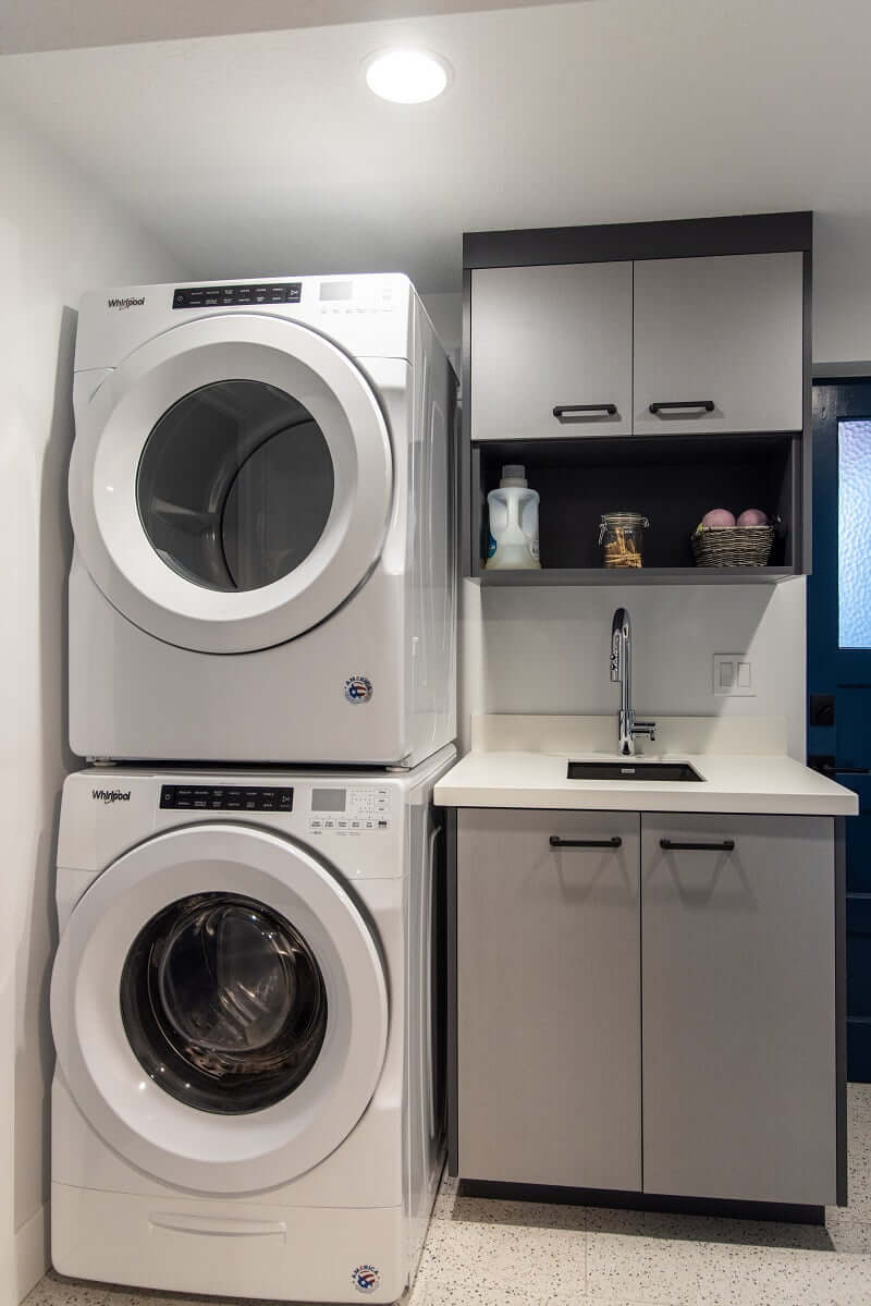 Compact laundry room with stacked washer and dryer next to a sink with cabinetry above.