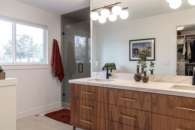 Contemporary bathroom remodel with two sinks next to the shower. Above the sink is a large mirror that is reflecting the closet and a picture on the wall behind. On the wall to the left is a towel hanging from a hook and a window.