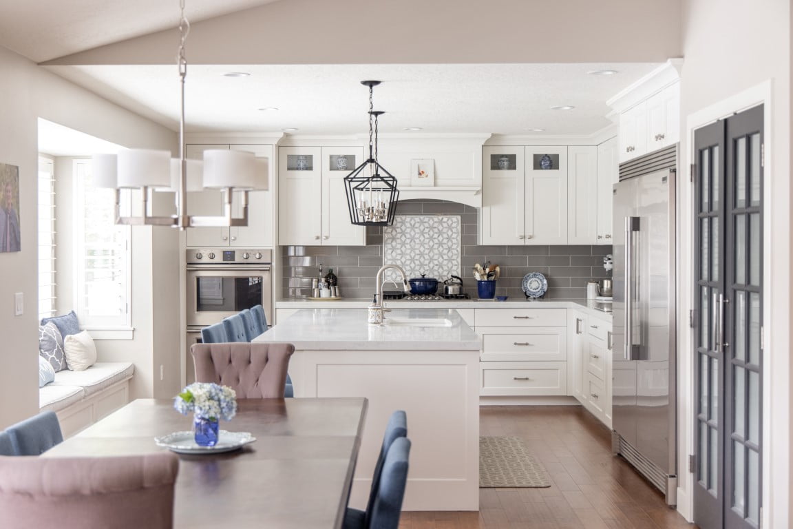 Modern Country kitchen renovation. The kitchen features a large fridge and freezer, island with seating and a sink, double ovens, gray tile backsplash, built-in bench seat, and open concept layout with the dining room.