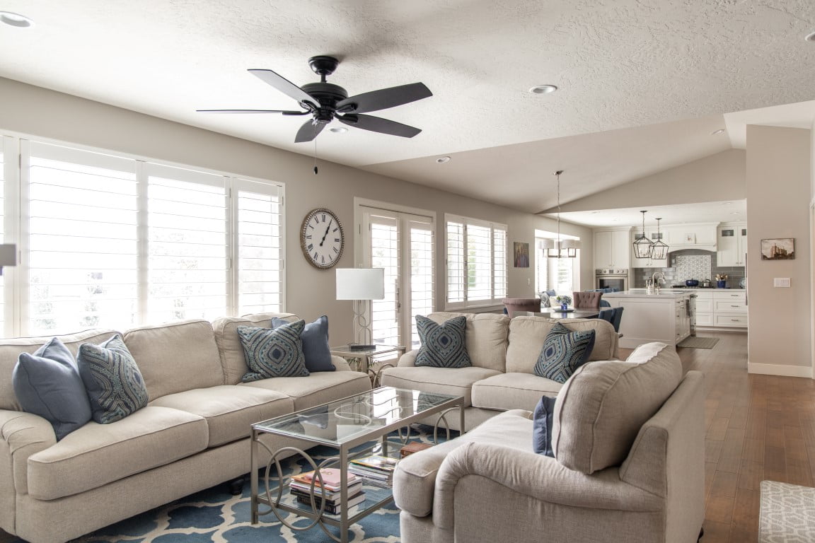 Open concept great room looking from the family room to the dining room and kitchen. The family room features two sofas and a chair around a coffee table with a ceiling fan above.