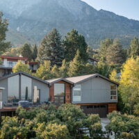 Thumbnail of http://Exterior%20of%20split%20level%20home%20after%20the%20renovation%20with%20a%20two-car%20garage,%20updated%20landscaping,%20and%20a%20modern%20railing%20leading%20up%20to%20the%20front%20porch%20and%20on%20the%20deck.%20The%20home%20sits%20in%20front%20of%20a%20beautiful%20mountain%20backdrop%20and%20is%20partially%20hidden%20by%20the%20landscaping.