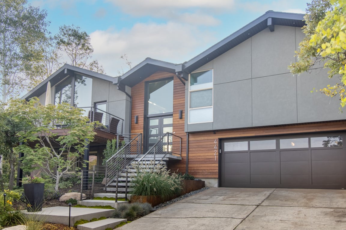 Exterior of split level home after the renovation with a two-car garage, updated landscaping, and a modern railing leading up to the front porch and on the deck.