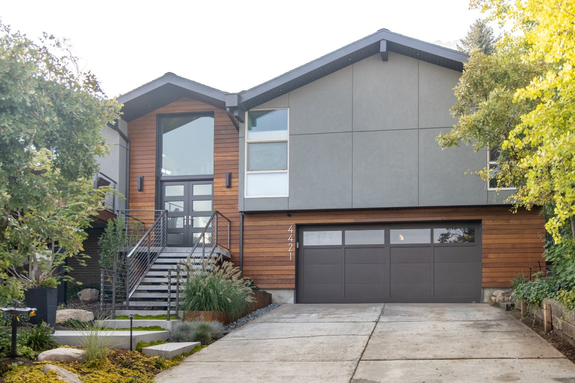 Exterior of split level home after the renovation with a two-car garage, updated landscaping, and a modern railing leading up to the front porch and on the deck.
