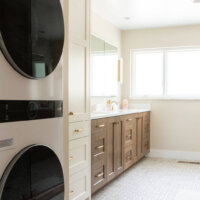 Thumbnail of http://Primary%20bathroom%20with%20a%20stacked%20washer%20and%20dryer,%20storage,%20double%20sinks,%20and%20large%20window.
