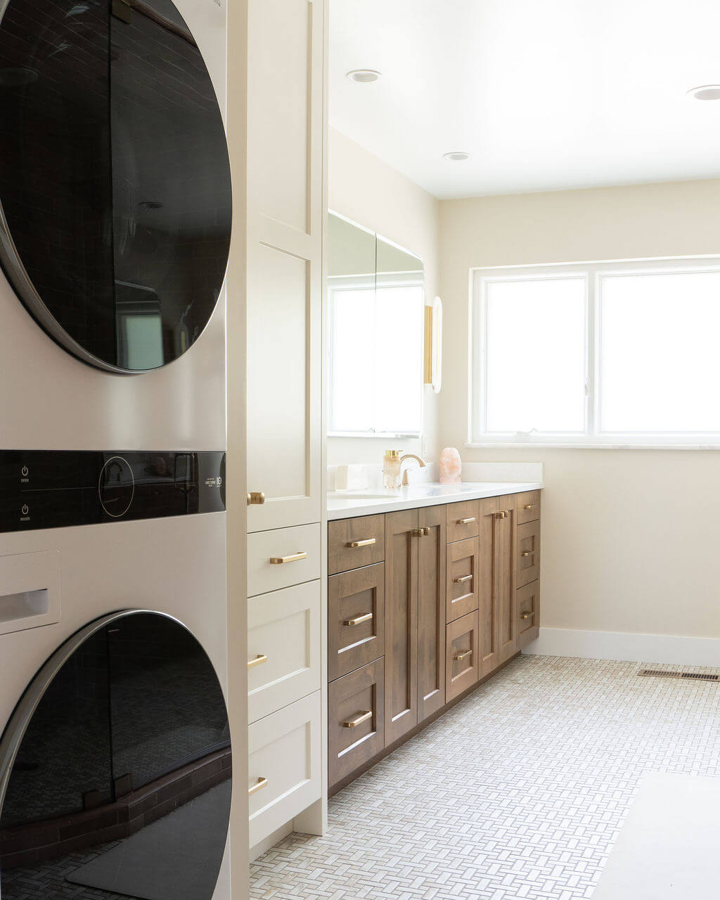 Primary bathroom with a stacked washer and dryer, storage, double sinks, and large window.