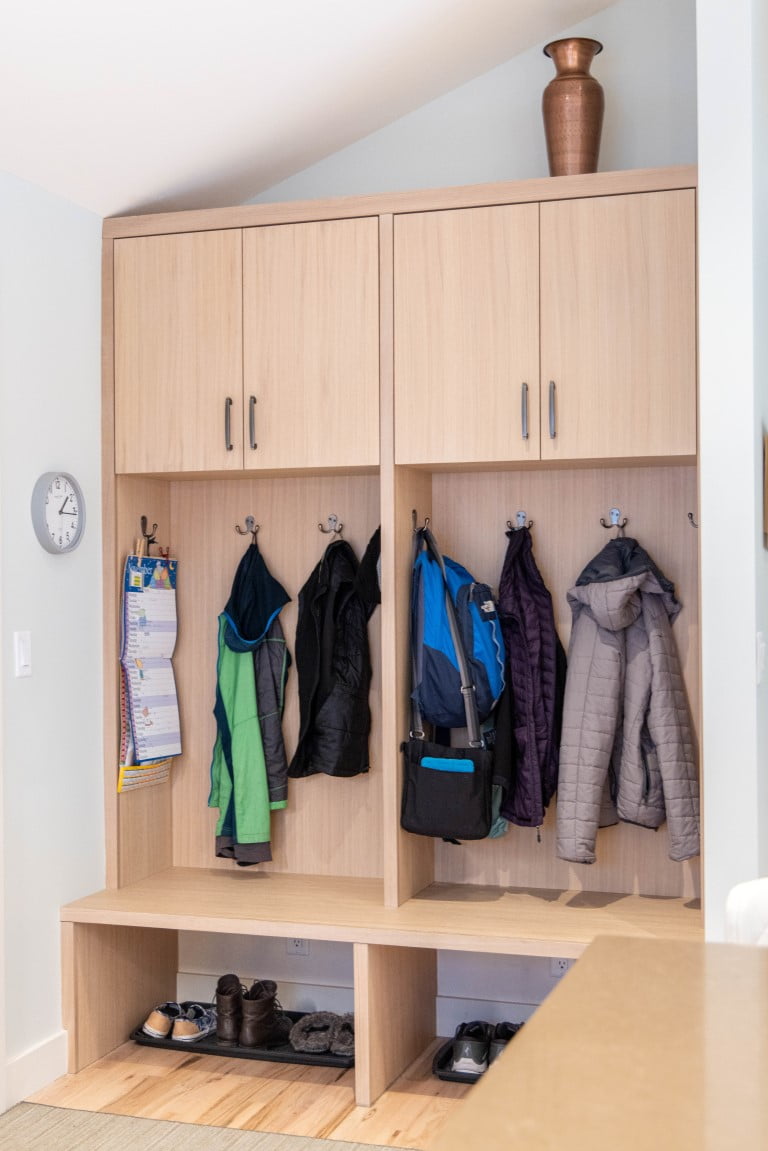 Modern mudroom cabinetry. The cabinets include open spots for shoes at the bottom, a bench with coat hooks behind on the wall, and cabinets above.