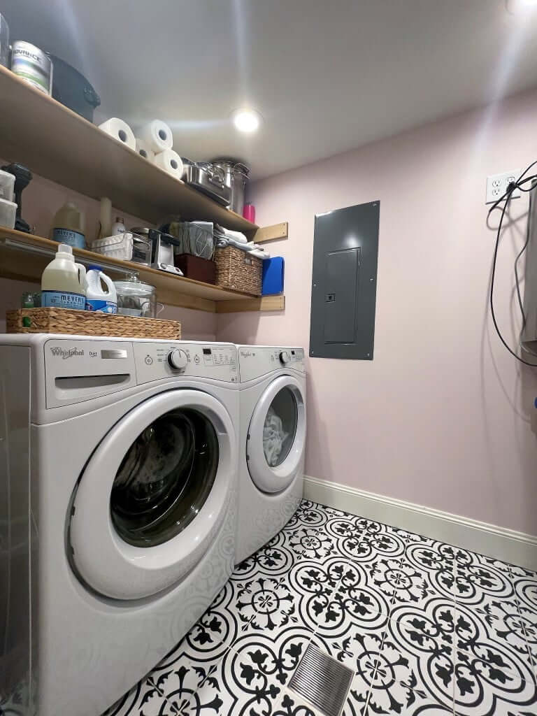 Laundry room with a side-by-side washer and dryer and open shelves above. The floor is tile with a pattern, and the walls are painted pink.