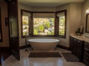 Large free standing bath tub in a bay window. In front of the tub are two small bath mats with one being in front of the sink. Across from the sink is an open door.