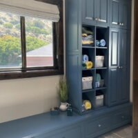 Thumbnail of http://Built-in%20cabinets%20painted%20blue.%20The%20built-ins%20include%20open%20shelving%20with%20baskets%20and%20rolled%20towels,%20a%20bench%20seat%20under%20the%20windows,%20and%20cabinets.