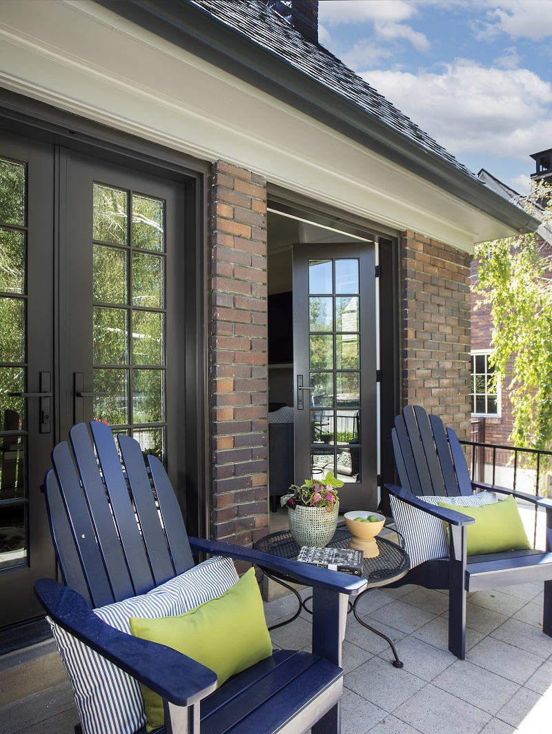 Front porch with french doors to the living room. On the front porch are two adirondack chairs and a round table between.