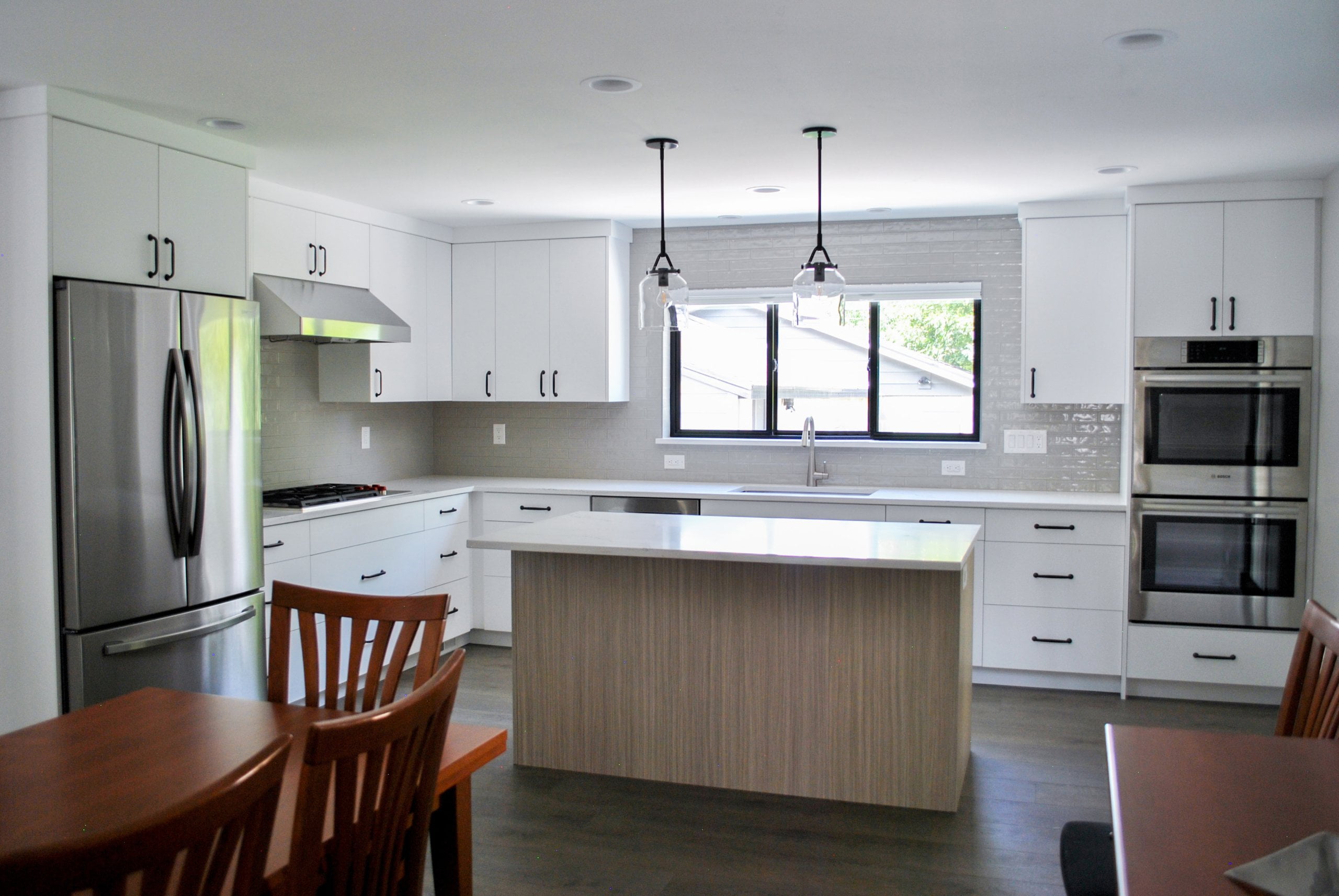 Open concept kitchen and dining room after the remodel. The kitchen is large and includes double ovens, an island with room for seating, and a sink under the window.