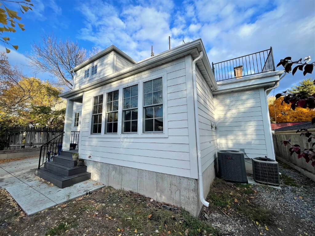 Exterior of a home addition. The addition includes white side paneling, stairs from a back porch, and a railing above.