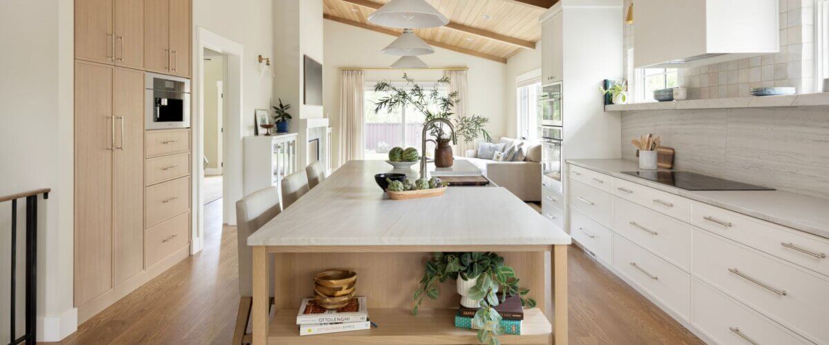Open concept kitchen with a large island in the center. On the right is a wall of cabinetry that includes the oven, stove, and fridge. In the center is a large island with open shelves on the end , the sink, and seating. On the left is a additional cabinetry with a built-in coffee machine.