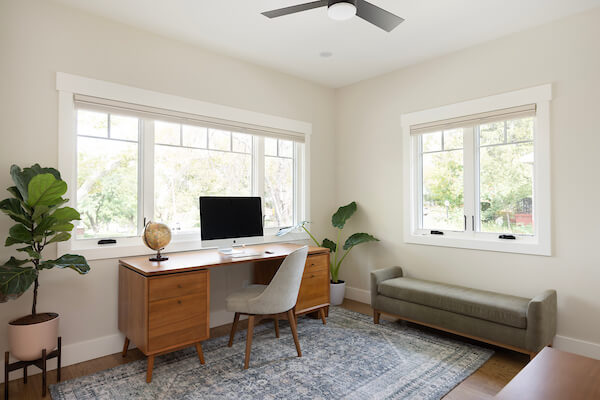 Home office furnished with a desk, plants, and bench seat.