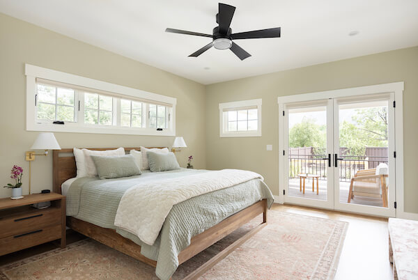 Primary bedroom with multiple windows, including two doors out to the back deck. The room is furnished with a bed, rug, and two nightstands.