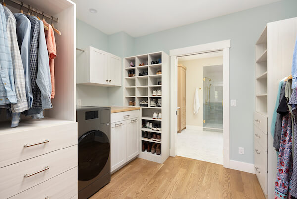Large walk-through primary closet. The closet features a combined washer and dryer, shoe storage, and plenty of hanging space for clothes. Straight ahead is the opening into the primary bathroom.