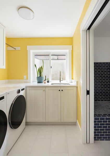 Laundry room in the basement with a window above the sink and yellow paint on the walls.